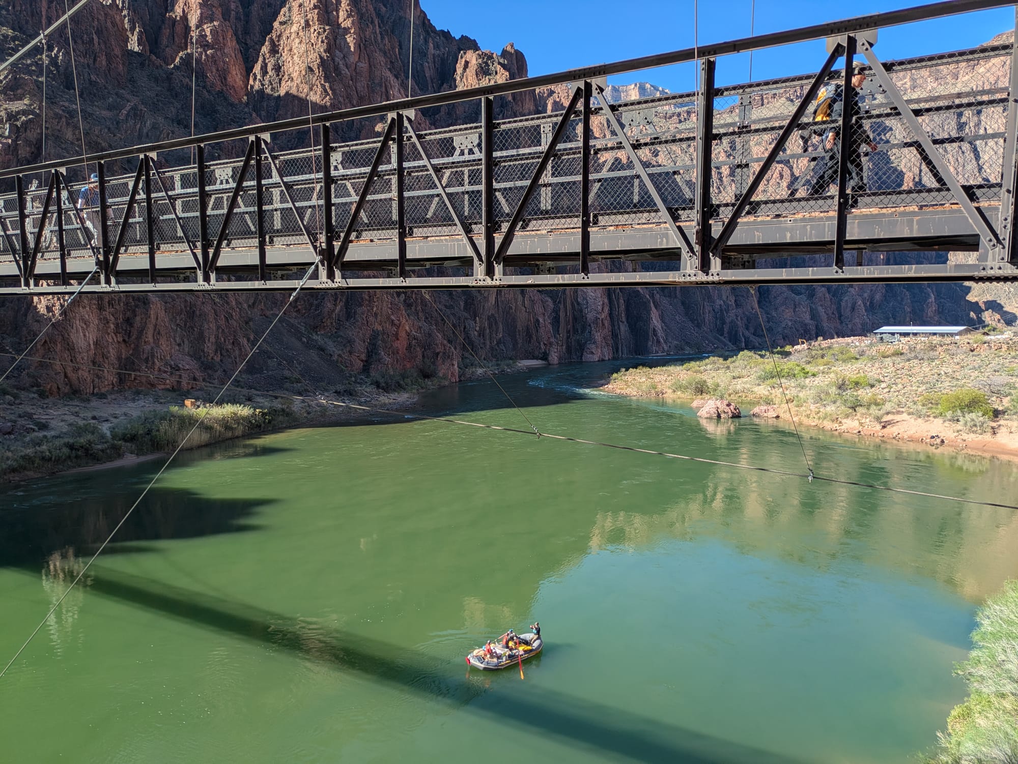A raft floats by under the Black Bridge that spans the Colorado river at the bottom of the Grand Canyon